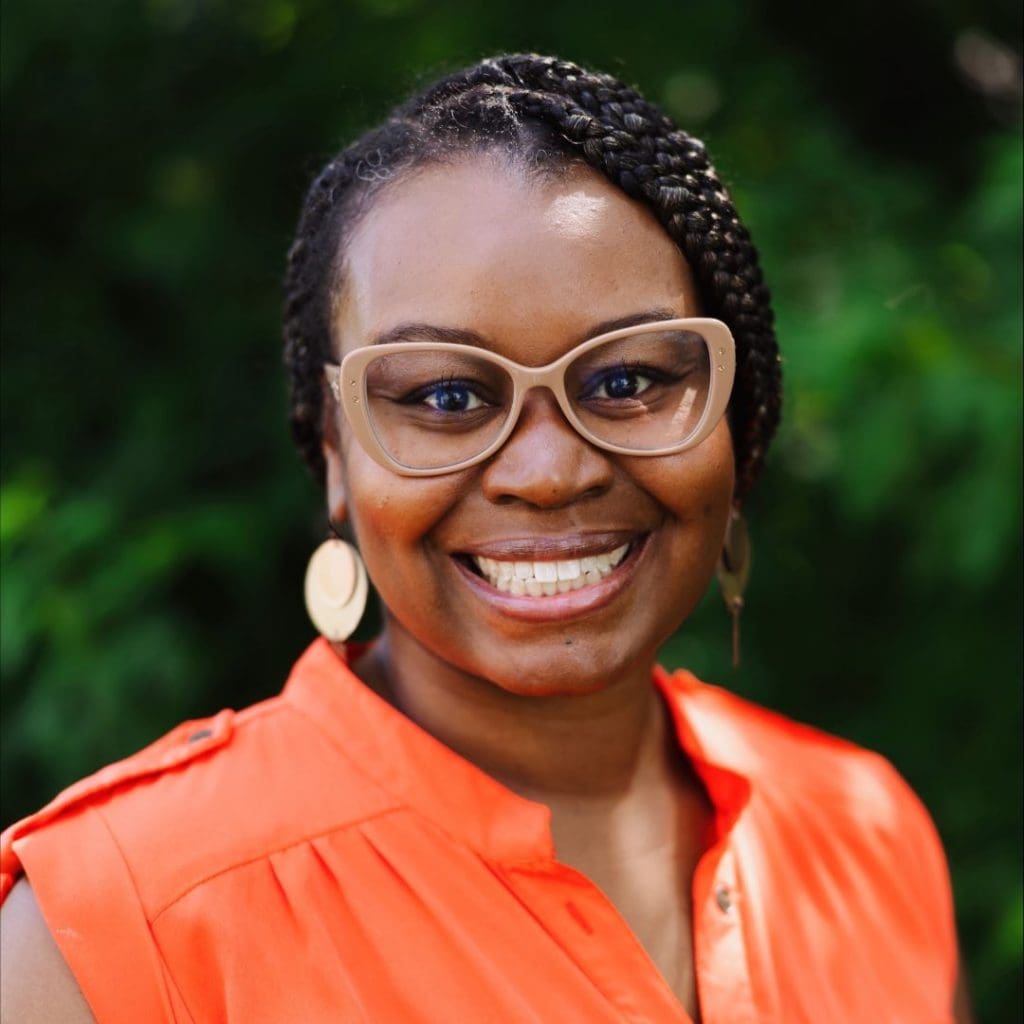 Black woman wearing glasses and an orange top, smiling