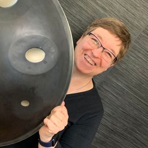 Woman with short brown hair wearing glasses and a black shirt holding a handpan