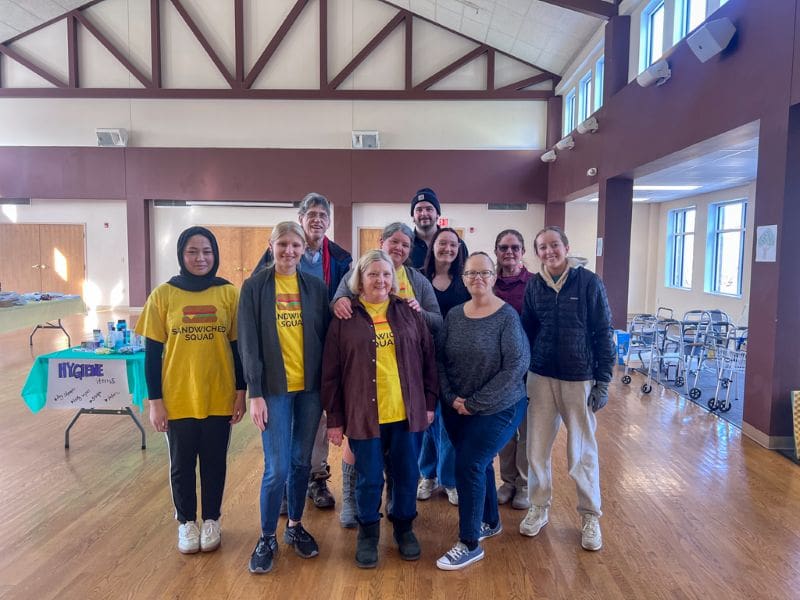 Group of volunteers wearing yellow shirts at an event with tables behind them