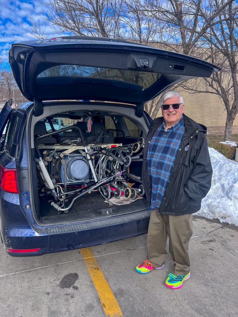 A man standing next to a van full of commodes and walkers